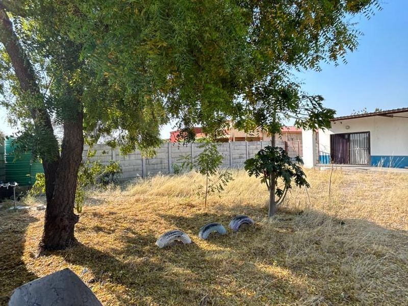 A spacious rear garden featuring mature trees, a precast concrete boundary wall, and a water tank, offering potential for landscaping and outdoor improvement.