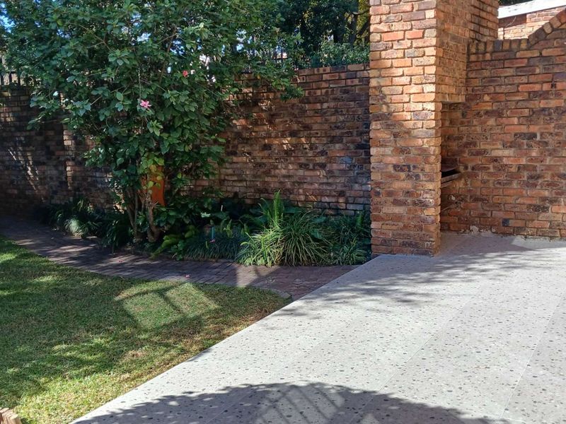 A private outdoor patio area featuring a built-in brick braai, paved flooring, and a landscaped garden with a brick boundary wall.