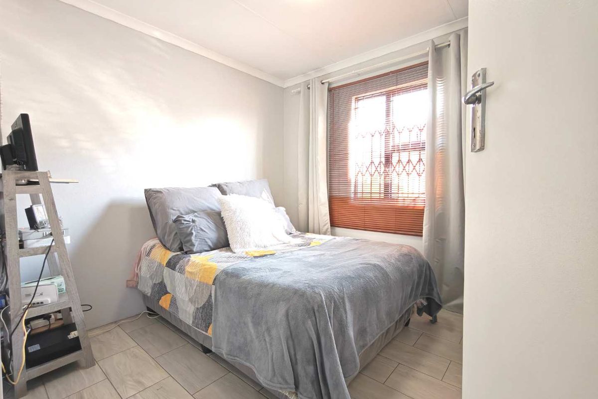 A well-maintained bedroom featuring neutral wall tones, tiled flooring, and a window fitted with security bars.