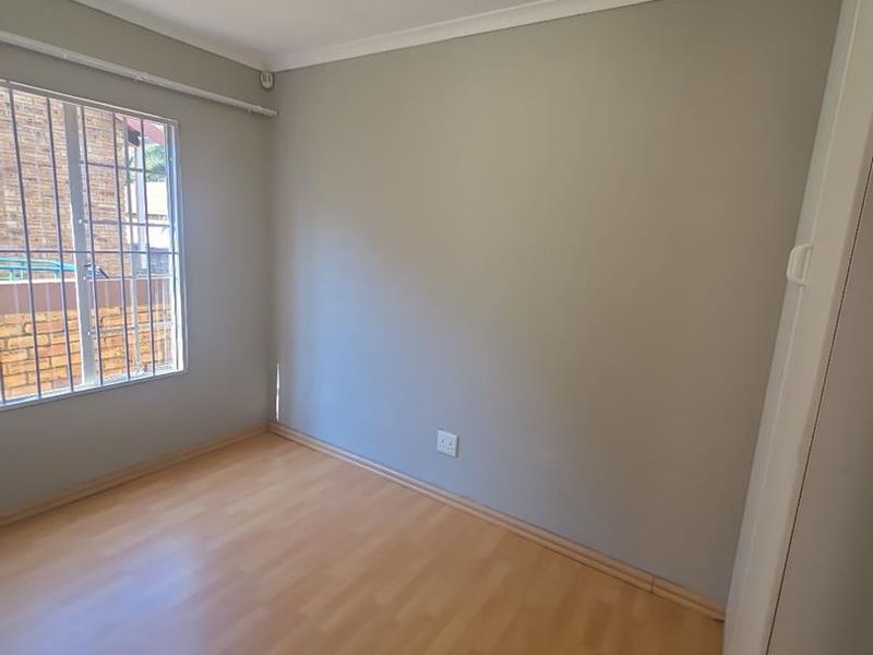 A clean, empty bedroom featuring light-toned laminate flooring, neutral walls, a built-in cupboard, and security bars on the window.