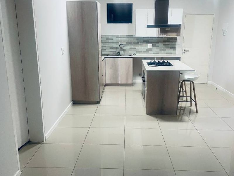 Modern kitchen featuring light wood-tone cabinetry, a central island with a gas hob, extractor fan, tiled backsplash, and neutral floor tiles.