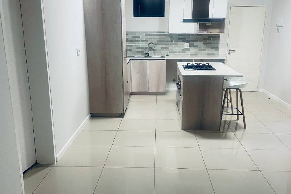 Modern kitchen featuring light wood-tone cabinetry, a central island with a gas hob, extractor fan, tiled backsplash, and neutral floor tiles.