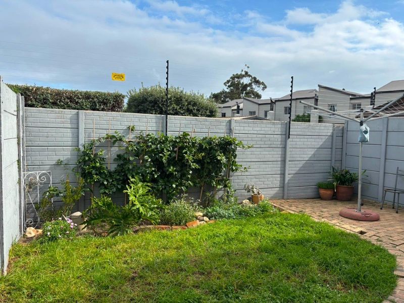 A private rear garden featuring a paved patio area, lawn, and secure boundary wall with electric fencing.