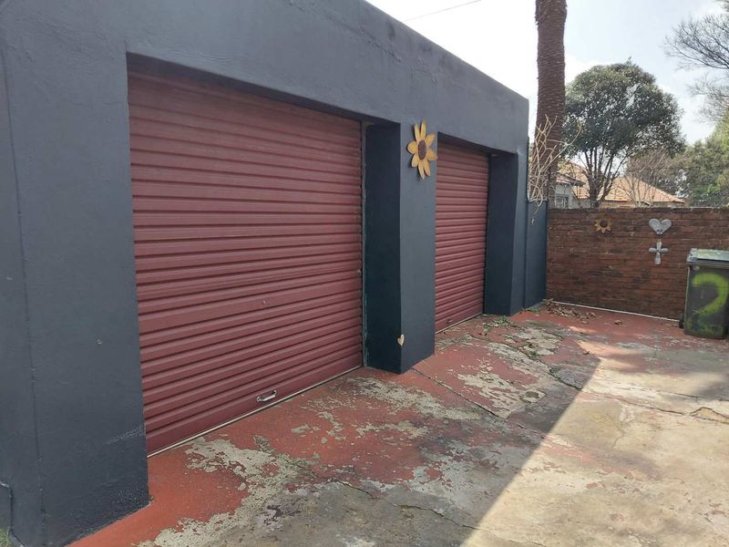 A double garage featuring red roller doors and a weathered concrete driveway area with a brick boundary wall.