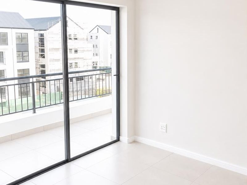 A bright, empty living area featuring neutral tiled floors, a modern pendant light, and large sliding glass doors leading to a private balcony.