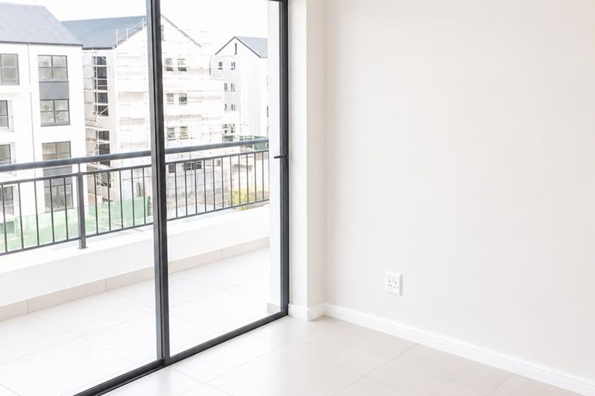 A bright, empty living area featuring neutral tiled floors, a modern pendant light, and large sliding glass doors leading to a private balcony.