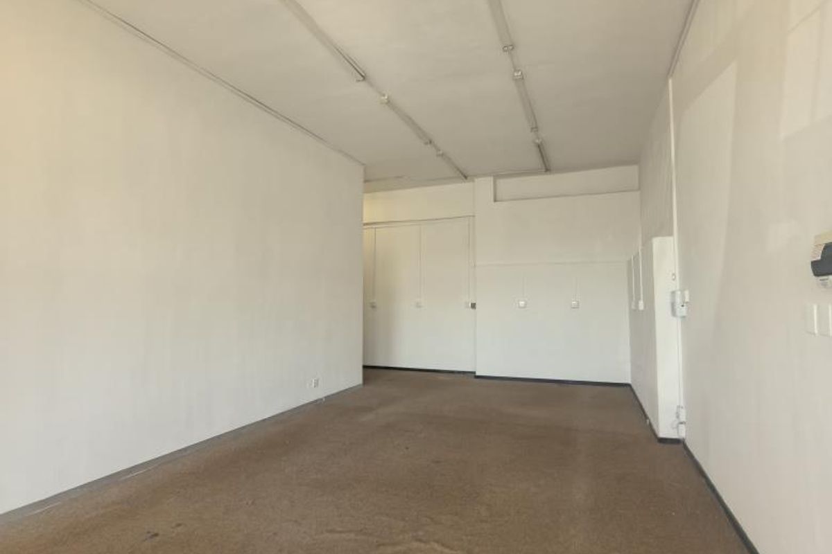An empty, open-plan office space featuring neutral walls, fluorescent strip lighting, and built-in storage cupboards with worn carpeting throughout.