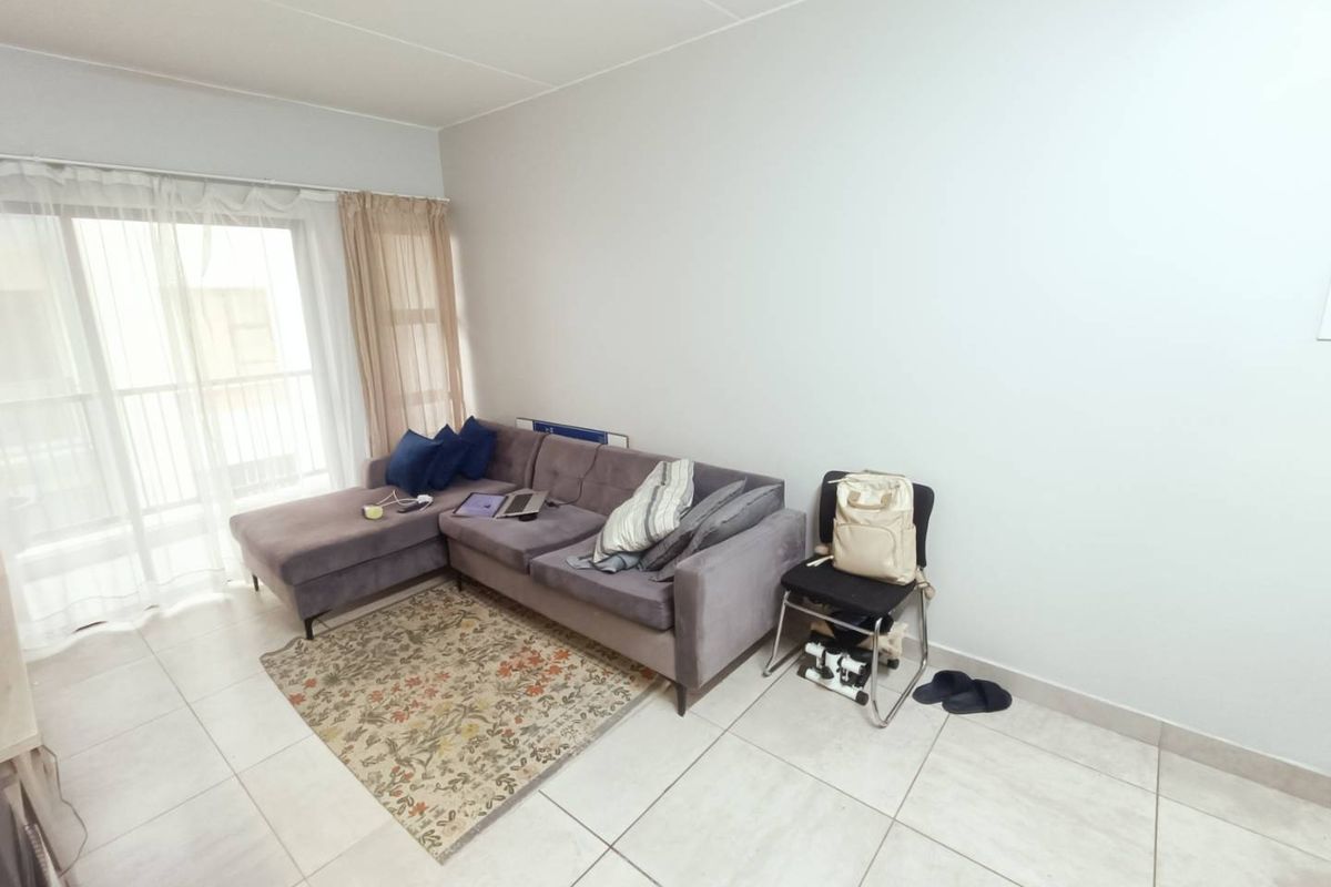 A bright living room featuring neutral floor tiles and a sliding glass door providing access to an outdoor balcony area.