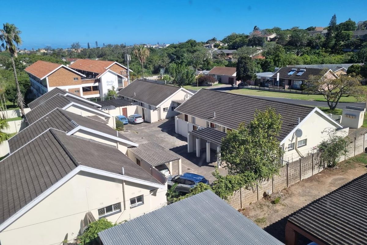 An elevated aerial view of a residential apartment complex featuring tiled roofs, paved driveways, and surrounding landscaped grounds.