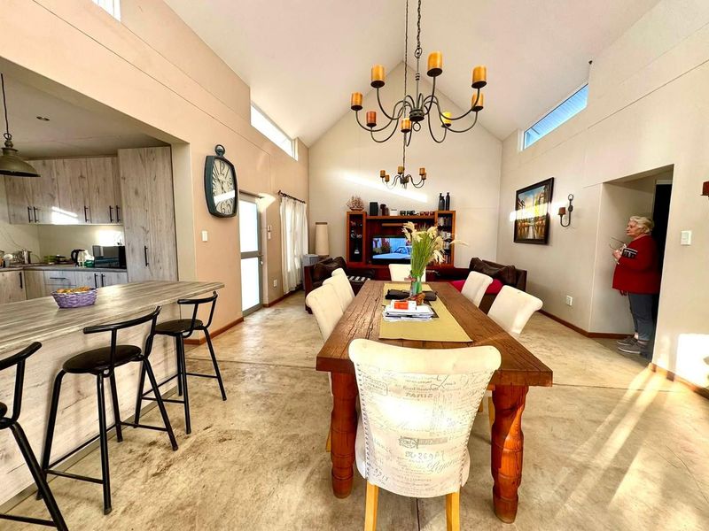 Spacious open-plan living and dining area featuring vaulted ceilings, clerestory windows, polished concrete floors, and a modern kitchen with a breakfast island.