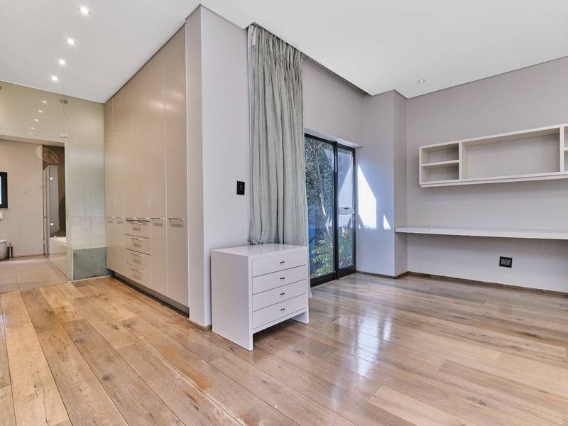 Spacious bedroom featuring hardwood flooring, extensive built-in cabinetry, a dedicated study area with floating shelves, and direct access to an en-suite bathroom.