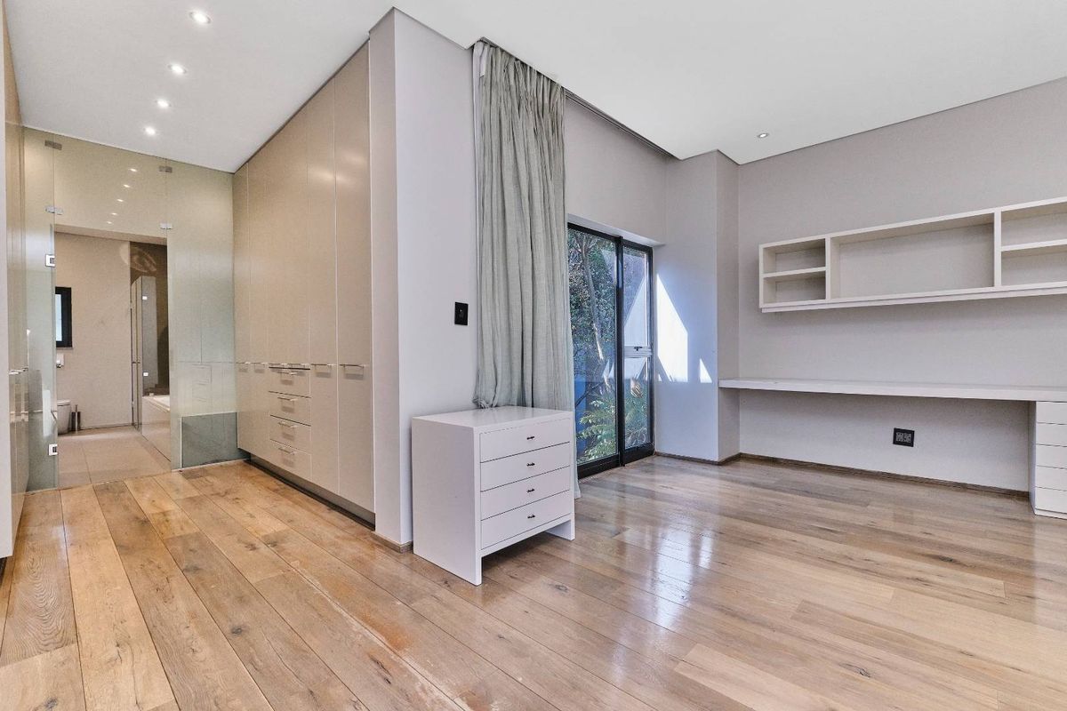 Spacious bedroom featuring hardwood flooring, extensive built-in cabinetry, a dedicated study area with floating shelves, and direct access to an en-suite bathroom.