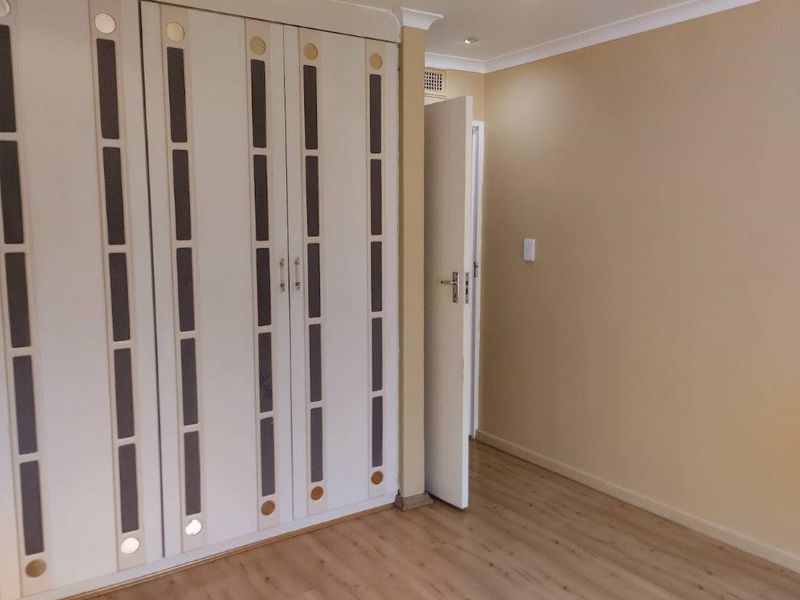 A clean, empty bedroom featuring light-toned laminate flooring and extensive built-in cupboards with decorative panel detailing.