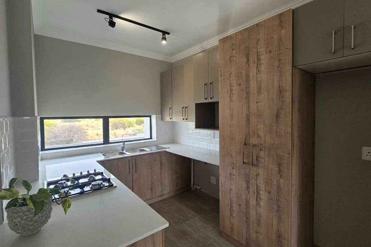 Modern kitchen featuring wood-look cabinetry, stone countertops, a built-in gas hob, double sink, and track lighting, offering a clean and functional workspace.