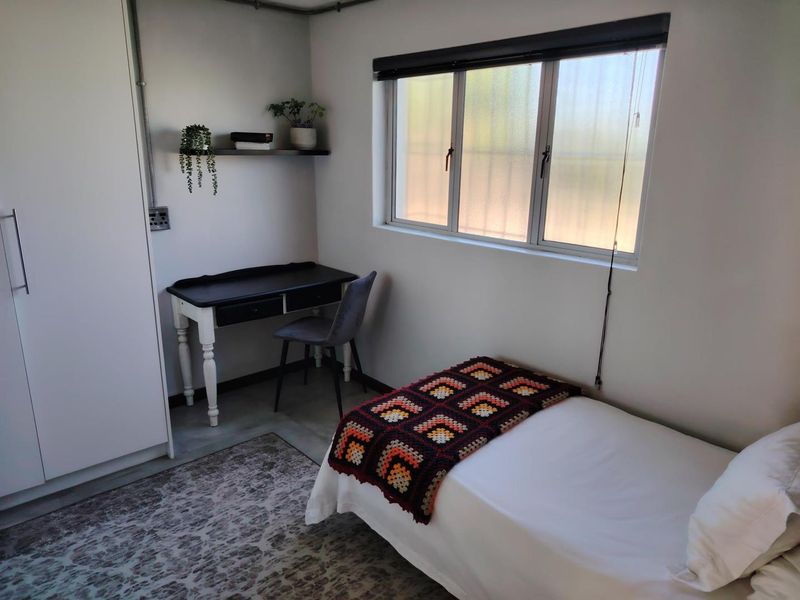 A compact bedroom featuring a built-in wardrobe, neutral walls, and a sliding window providing natural light.
