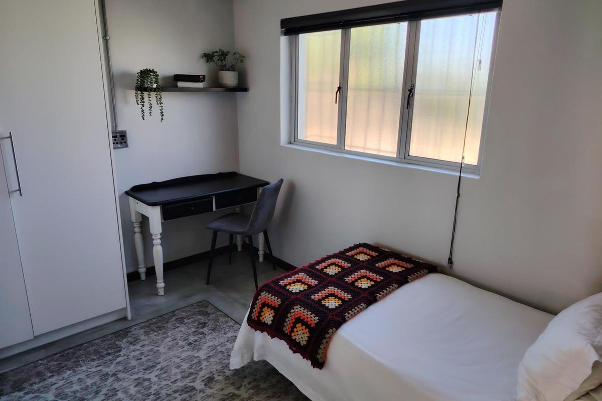 A compact bedroom featuring a built-in wardrobe, neutral walls, and a sliding window providing natural light.