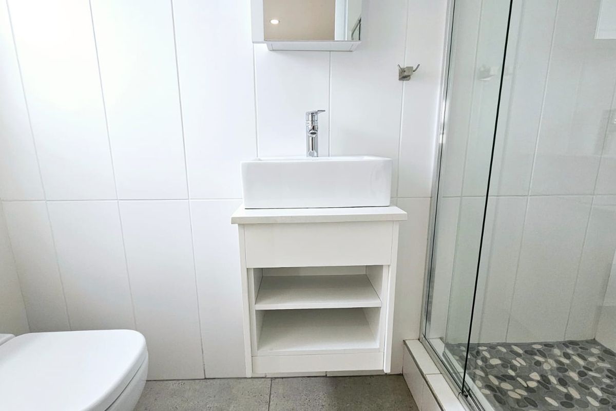 A clean, modern bathroom featuring a white vessel sink vanity, glass-enclosed shower with pebble flooring, and wall-mounted medicine cabinet.