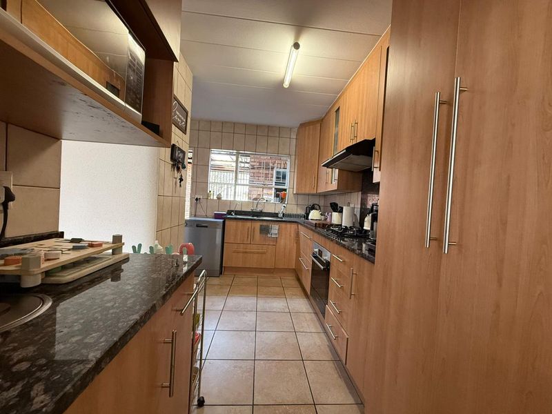 A functional galley-style kitchen featuring light wood cabinetry, granite countertops, a built-in oven, gas hob, and tiled flooring with a window for natural light.