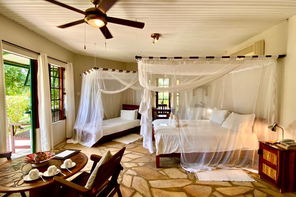 Spacious lodge bedroom featuring unique stone flooring, a corrugated ceiling with a fan, and large windows providing natural light and garden access.