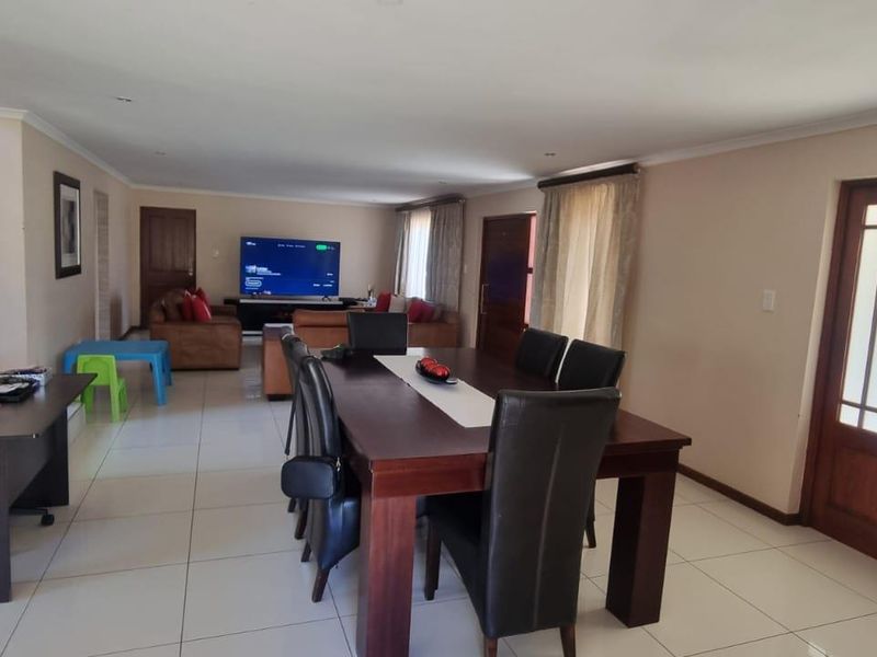 Spacious open-plan living and dining area featuring large format floor tiles, recessed lighting, and double wooden entrance doors.