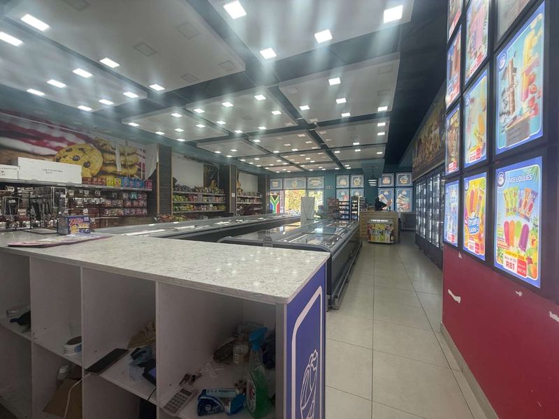 A commercial retail space featuring tiled flooring, recessed ceiling lighting, built-in service counters, and multiple commercial refrigeration units for product display.