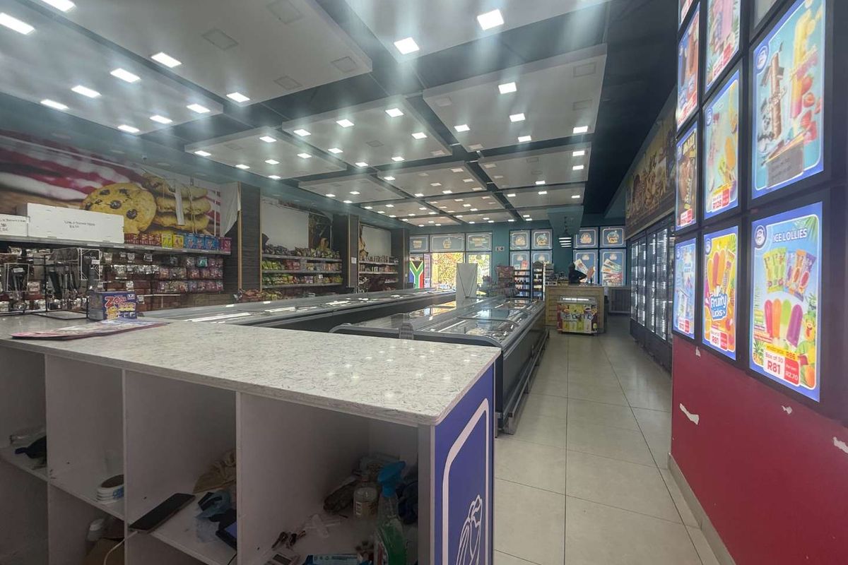 A commercial retail space featuring tiled flooring, recessed ceiling lighting, built-in service counters, and multiple commercial refrigeration units for product display.