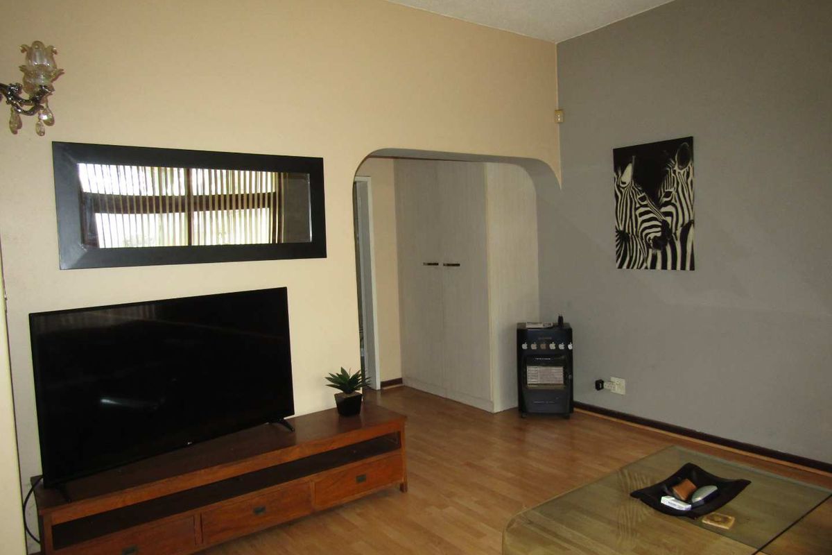 A living room featuring laminate flooring, an arched doorway leading to a hallway, and built-in storage cupboards.
