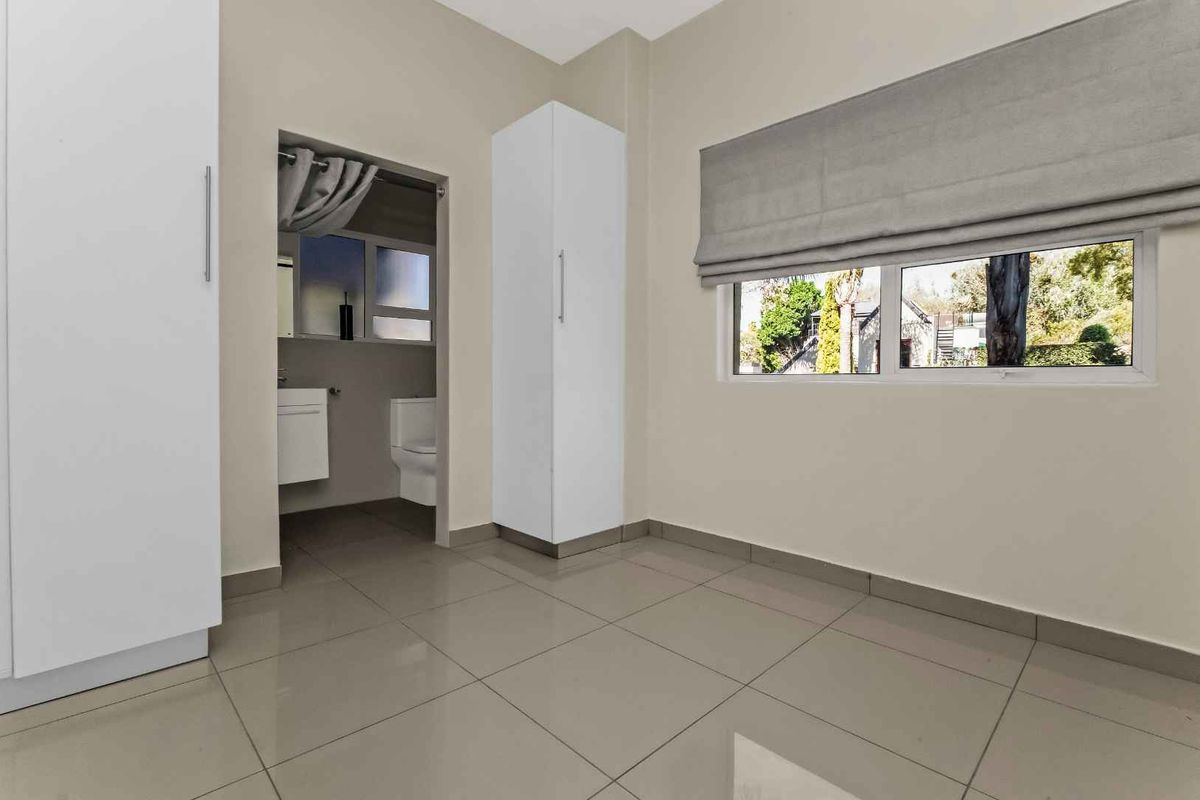 A bright, empty bedroom featuring neutral tiled flooring, built-in white cabinetry, and an en-suite bathroom with modern fixtures.