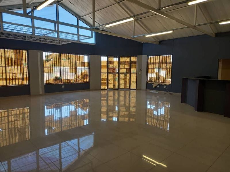 Spacious open-plan industrial unit featuring polished tiled flooring, exposed steel roof trusses, and a built-in reception counter, offering a clean and versatile workspace.