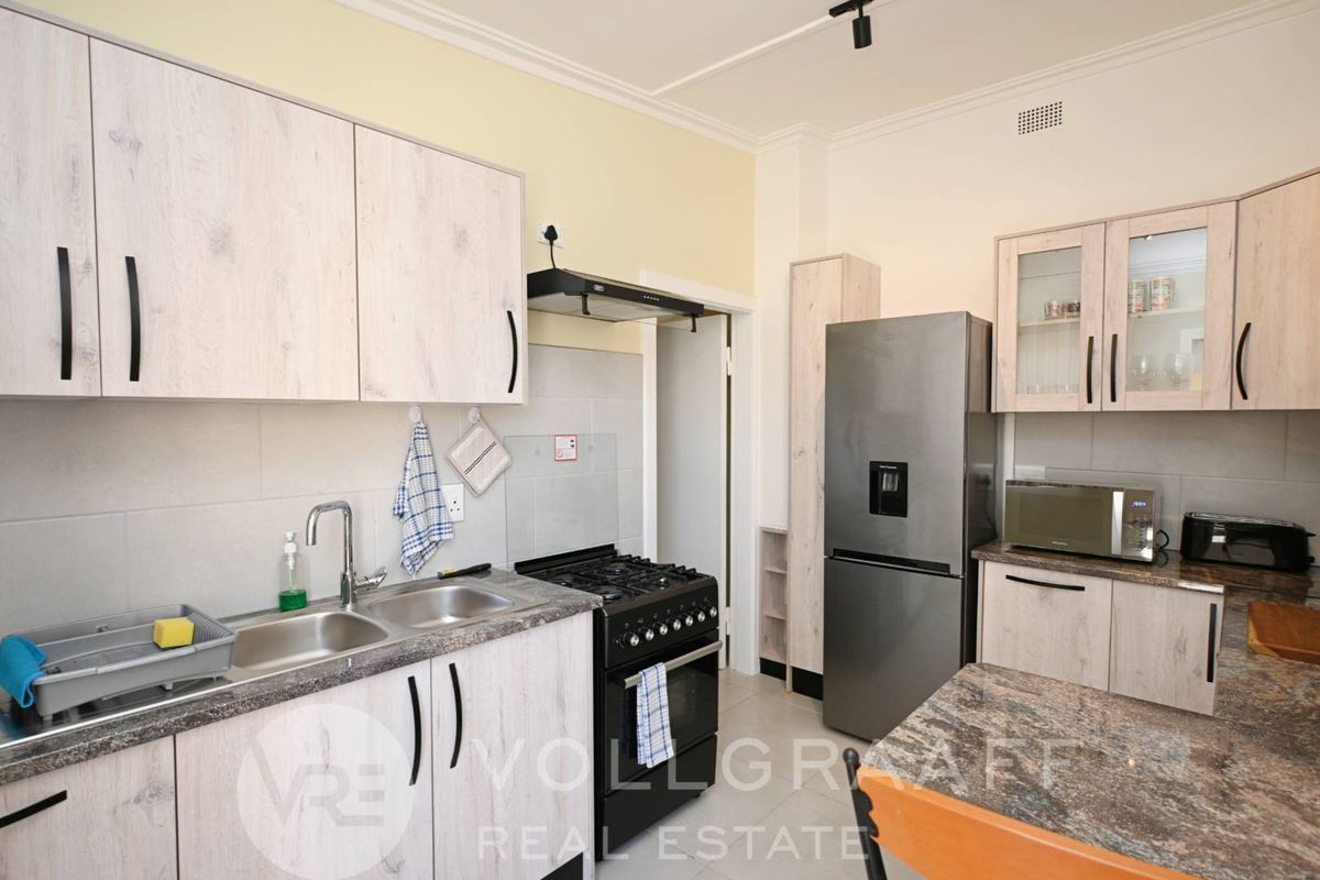A functional kitchen featuring light wood-grain cabinetry, stone-look countertops, a double sink, and a built-in gas stove with an extractor fan.