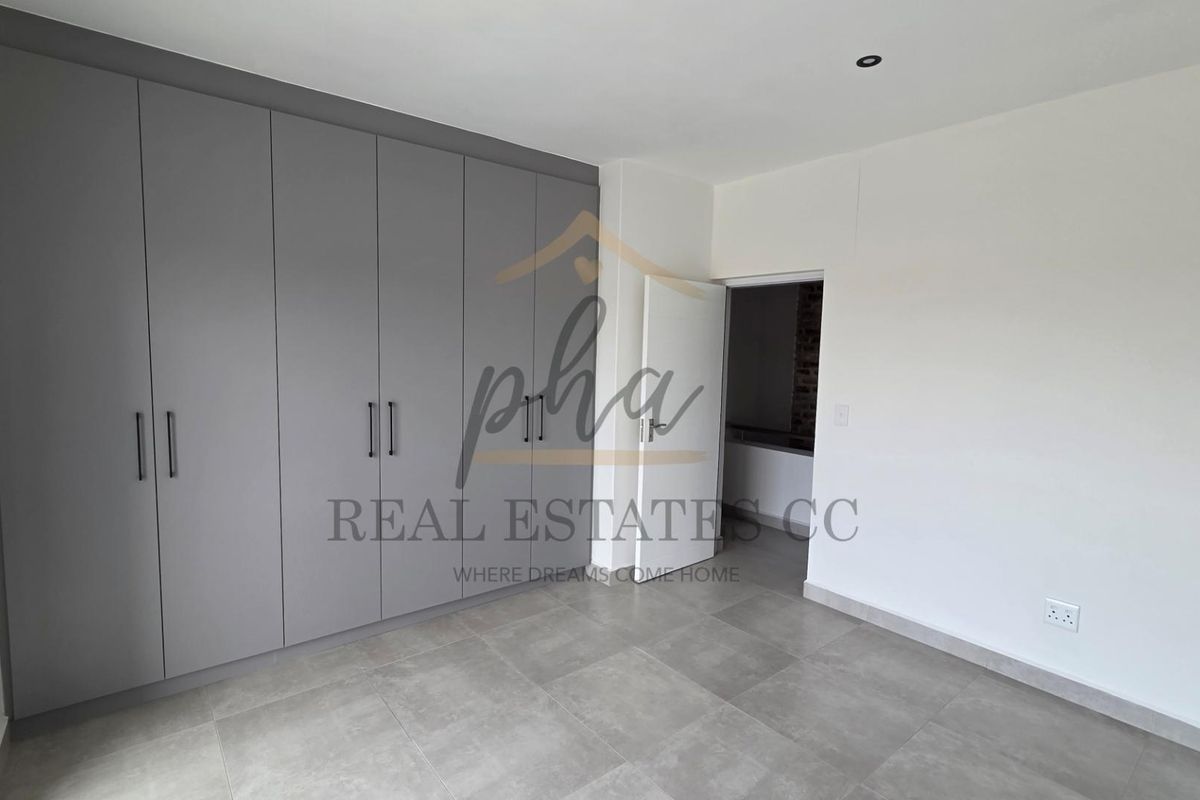 A modern bedroom featuring neutral grey floor tiles and extensive built-in floor-to-ceiling cabinetry with sleek handles.
