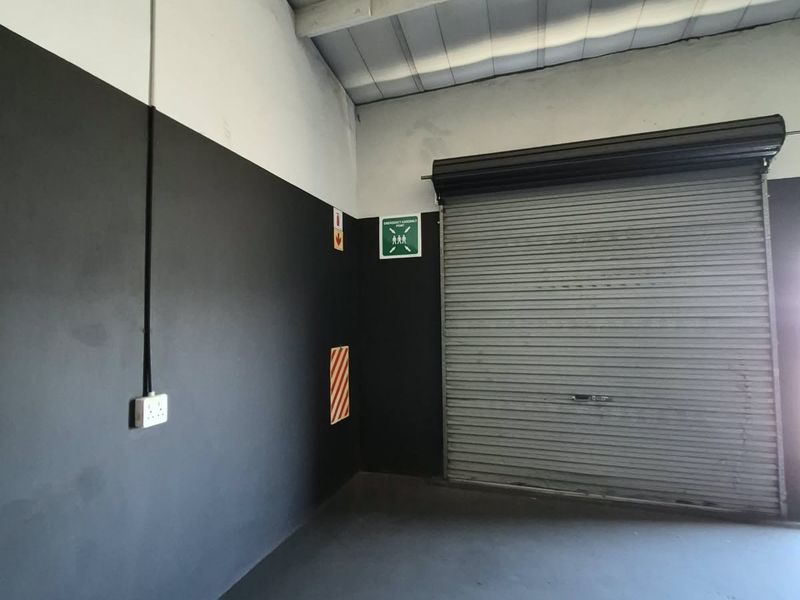 A clean, industrial-style garage space featuring a secure roller shutter door, exposed ceiling beams, and functional electrical infrastructure.