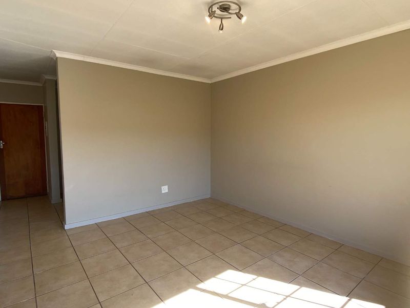 An empty living room featuring neutral wall paint, ceramic floor tiles, and a ceiling-mounted light fixture.