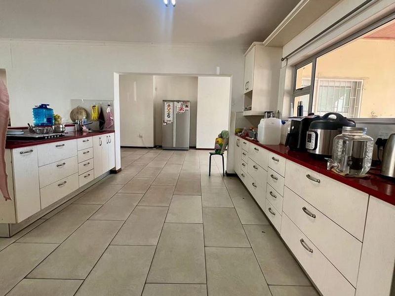 A functional kitchen featuring extensive white cabinetry, contrasting countertops, and large format floor tiles, offering a clean and practical layout for daily use.