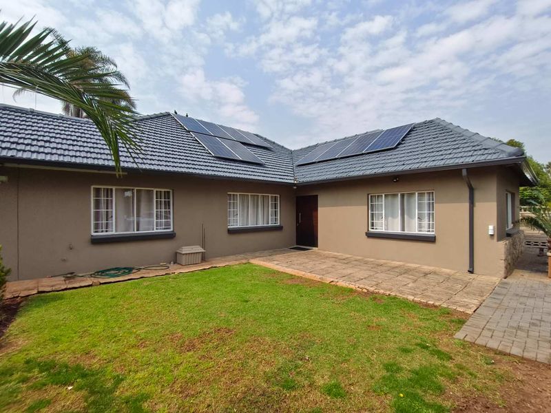 Rear view of the house featuring a paved patio, well-maintained lawn, and roof-mounted solar panels.