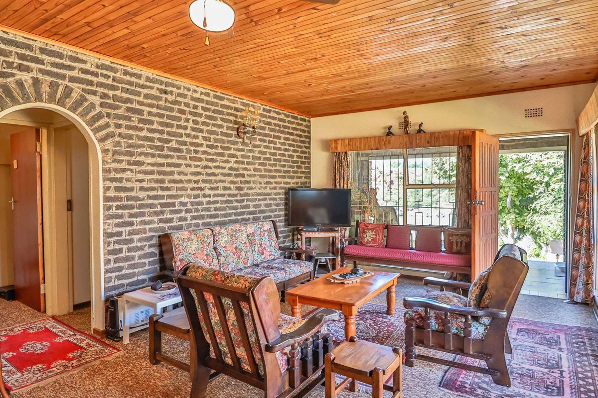 A living room featuring a rustic exposed brick feature wall, timber-clad ceiling, and large windows providing natural light and access to the outdoor area.
