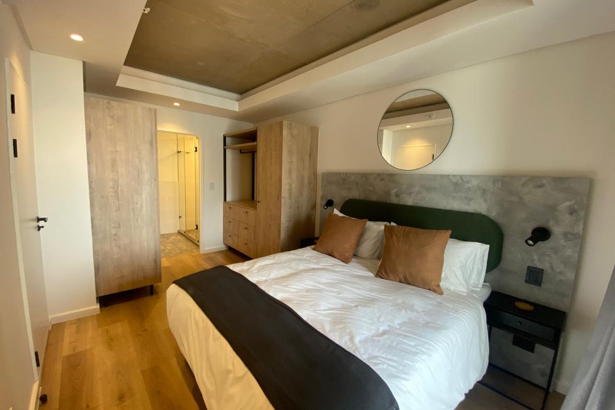 Modern bedroom featuring a recessed ceiling, wood-look flooring, built-in cabinetry, and an en-suite bathroom with contemporary finishes.