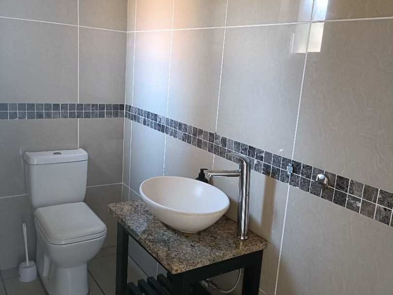 A clean, modern bathroom featuring neutral wall tiles with a mosaic accent border, a granite-topped vanity with a vessel sink, and a standard toilet.