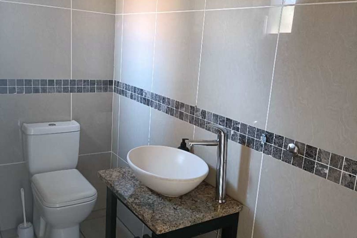 A clean, modern bathroom featuring neutral wall tiles with a mosaic accent border, a granite-topped vanity with a vessel sink, and a standard toilet.