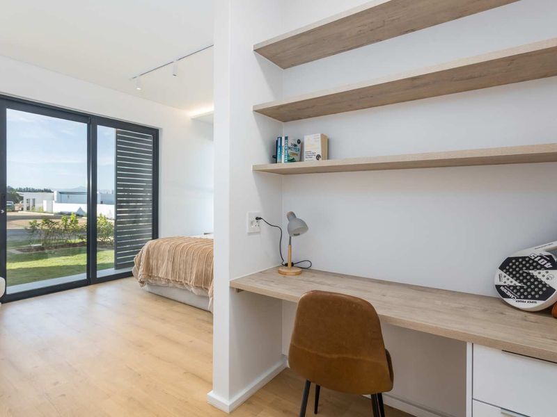 Modern bedroom featuring a built-in study nook with floating shelves, laminate flooring, and large sliding glass doors providing access to the exterior.