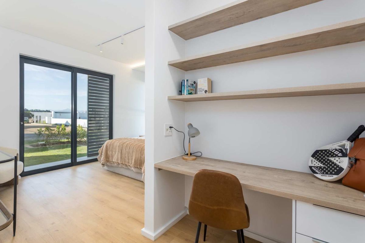 Modern bedroom featuring a built-in study nook with floating shelves, laminate flooring, and large sliding glass doors providing access to the exterior.