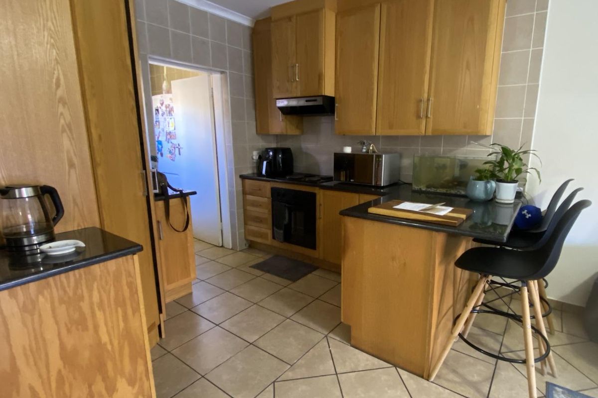 A functional kitchen featuring wooden cabinetry, dark countertops, tiled flooring, and a breakfast bar area.