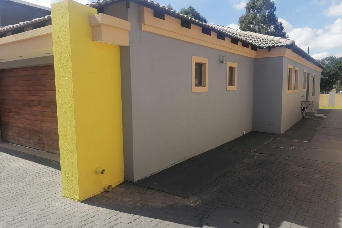 Rear exterior view of the property featuring a paved driveway, garage access, and a well-maintained rendered facade with contrasting yellow accents.