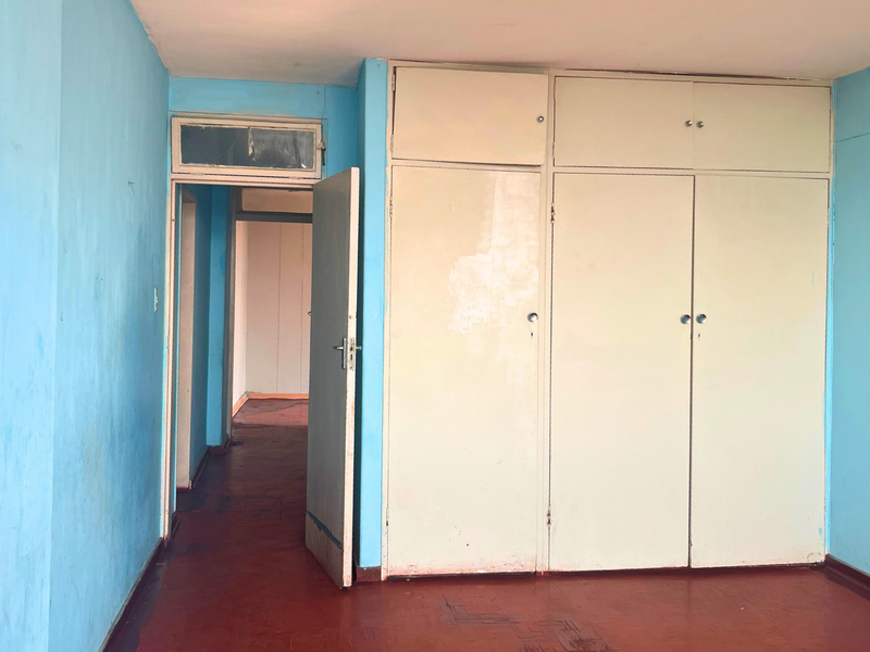 Empty bedroom featuring built-in cupboards, original parquet flooring, and a transom window above the doorway, offering a blank canvas for renovation.