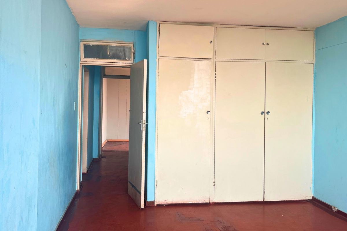 Empty bedroom featuring built-in cupboards, original parquet flooring, and a transom window above the doorway, offering a blank canvas for renovation.