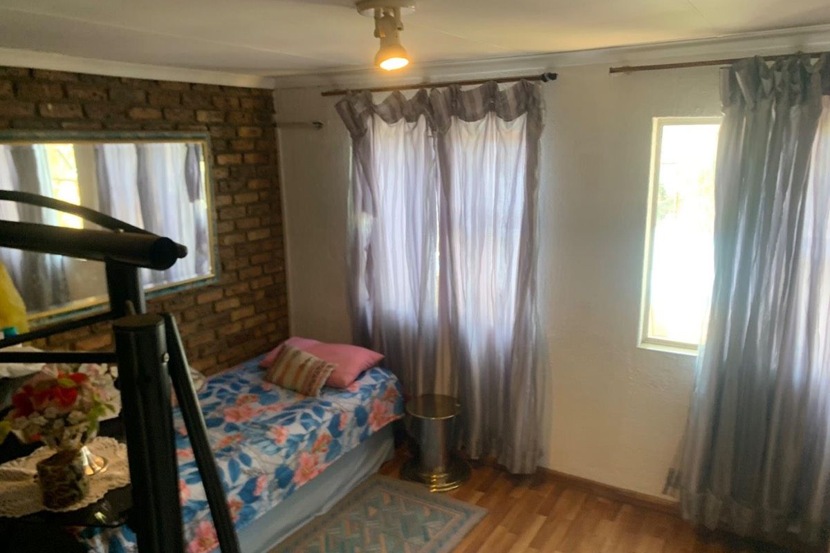 A bedroom featuring a rustic exposed brick feature wall, laminate flooring, and natural light through two windows.