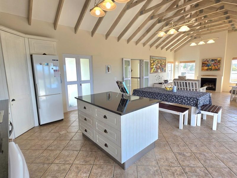 Spacious open-plan living area featuring a vaulted ceiling with exposed rafters, a central kitchen island with granite countertops, and a cozy built-in fireplace.
