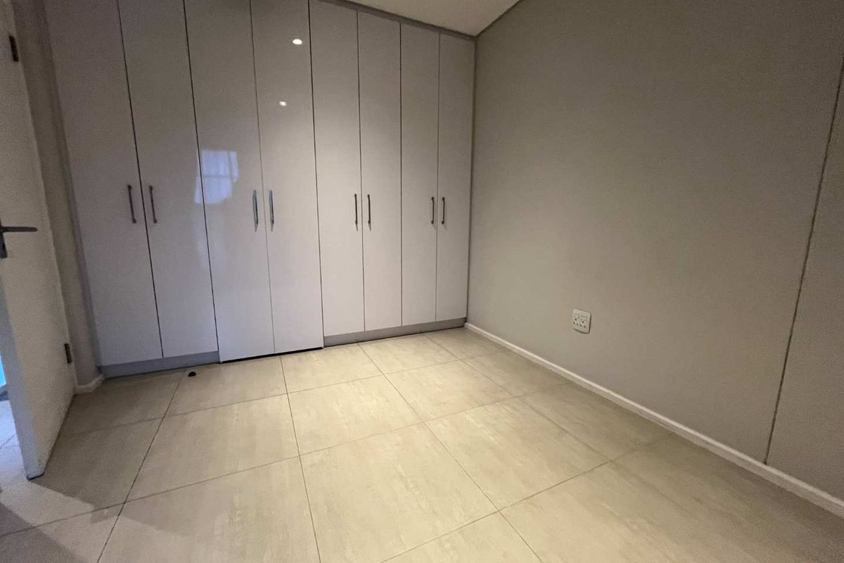 A clean, modern bedroom featuring large, white built-in cupboards and neutral tiled flooring, offering a bright and minimalist living space.