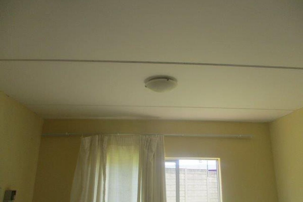A simple bedroom interior featuring a ceiling light fixture and a curtain rod above the window.