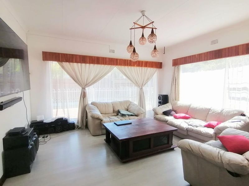 A spacious living room featuring light-toned laminate flooring, wooden pelmets, and a decorative pendant light fixture, offering a comfortable and functional living space.